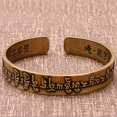 Vintage brass open cuff bracelet with raised Tibetan Sanskrit mantra exterior and interior Chinese characters Om Bolo and Svaha on beige linen background