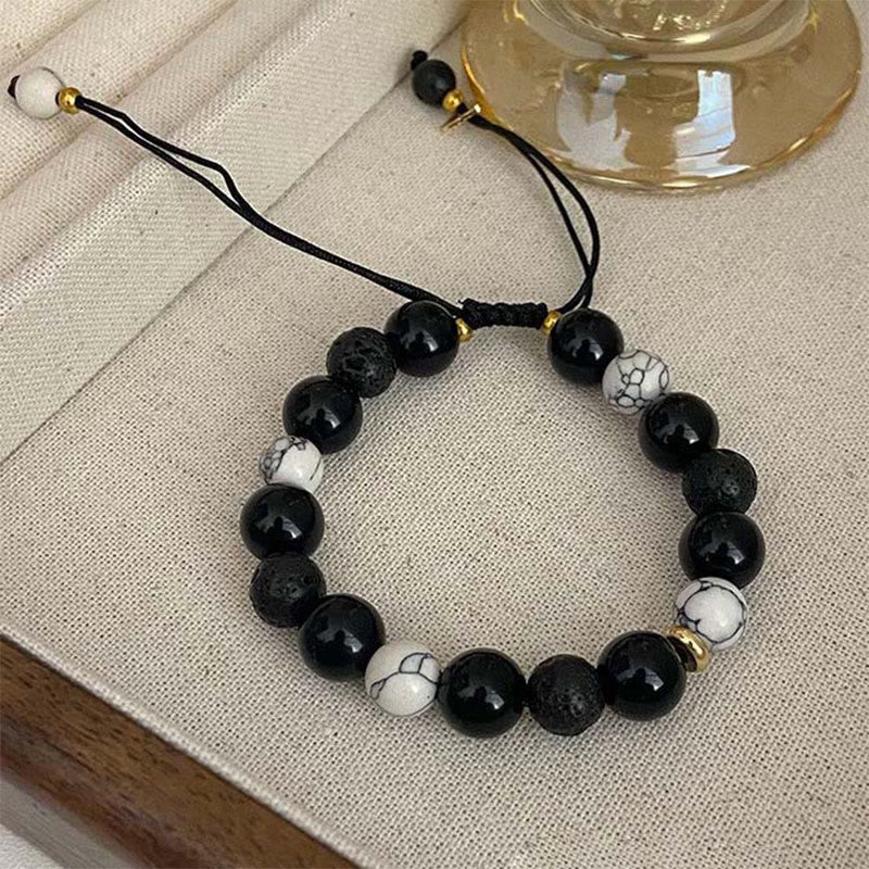 Black Obsidian Lava Rock Yin Yang Bracelet - angled on linen fabric with amber glass, adjustable cord, gold spacers