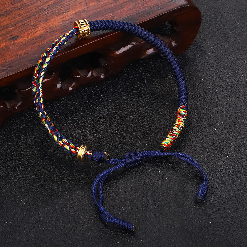 Om Mani Padme Hum Red String Bracelet – Deep blue adjustable bracelet with five-color woven sections and gold bead on black background with carved wood prop