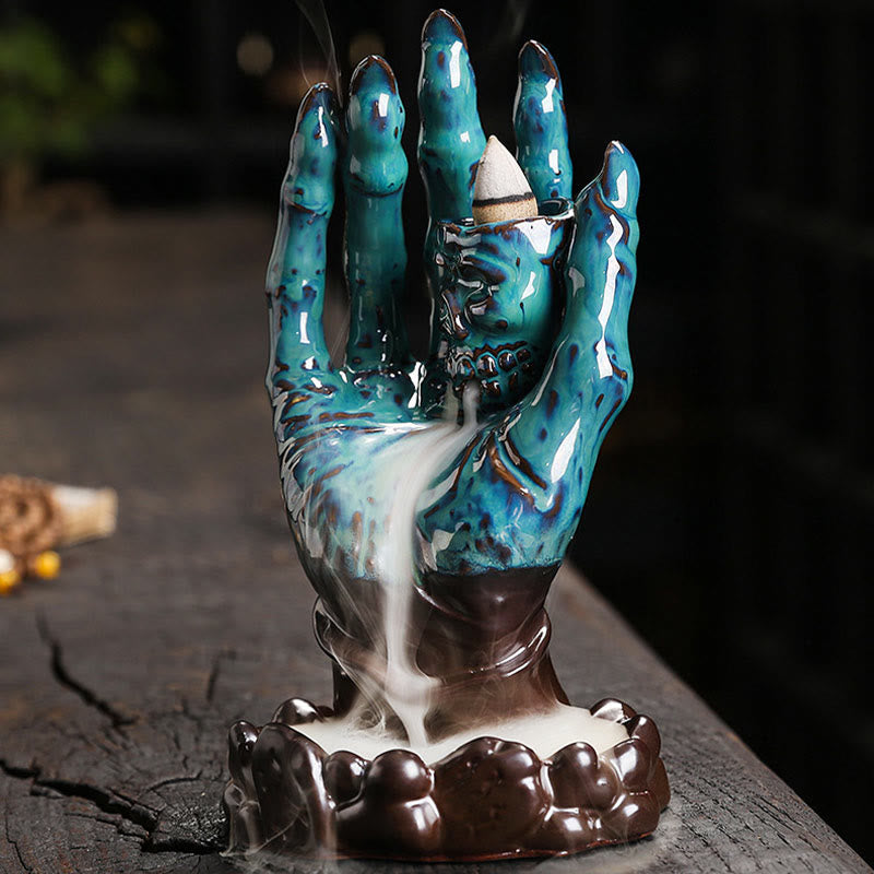 Ceramic Ghost Hand Skull Incense Burner – Turquoise hand with skull on lotus base, backflow smoke flowing down, greenery bg