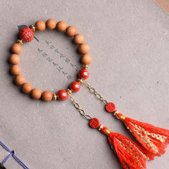 Peach Wood PiXiu Wealth Bracelet – Sandalwood and cinnabar beads with red tassels on gray paper, feng shui