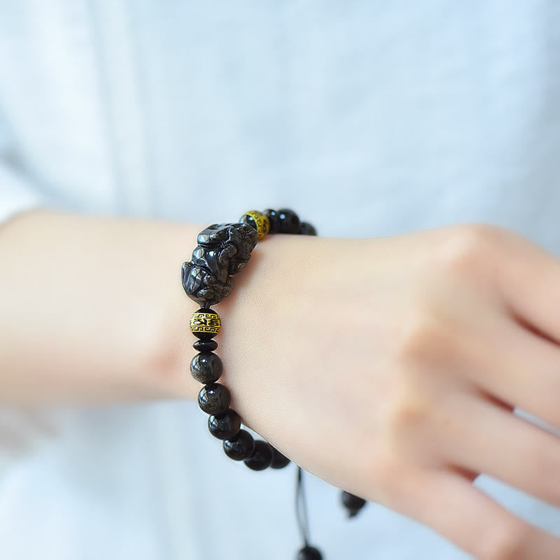 Gold Sheen Obsidian Pixiu Bracelet – Low angle on dark fabric highlighting stone luster, cord bracelet