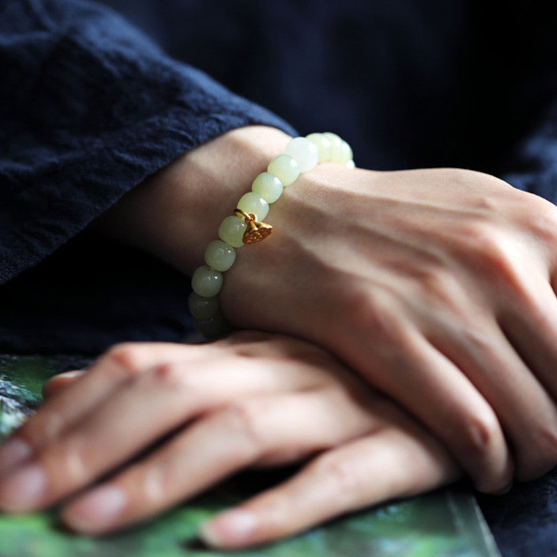 Jade Lotus Abundance Bracelet – On wrist over navy silk with gold lotus accent, warm lighting, jade lotus jewelry