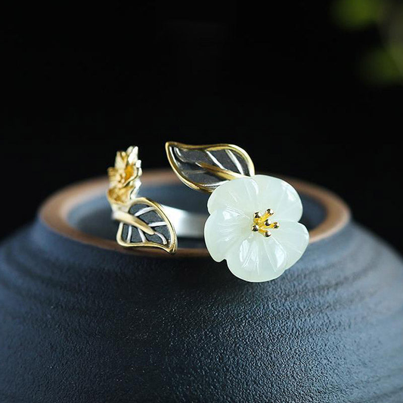 White Jade Plum Blossom Silver Ring - Open ring on dark ceramic vessel with white jade plum blossom, gold stamen center, gold flower bud, and silver leaves