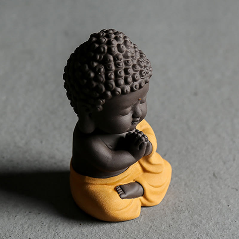 Small Buddha Purple Clay Decoration – three-quarter side view on concrete, yellow-robe variant, elevated angle, artisan colle
