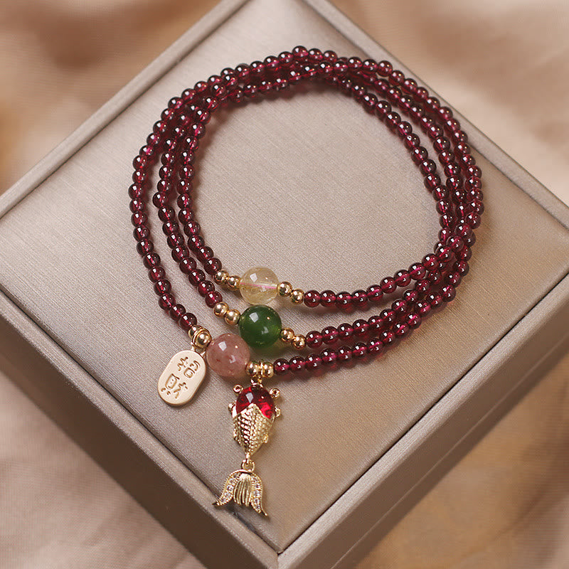 Garnet wrap bracelet with koi fish pendant red crystal body textured gold scales and zhao cai attract wealth charm tag on taupe satin-lined jewelry gift box display