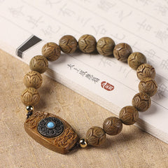 Green Sandalwood & Ebony Soothing Bracelet – angled view beside traditional scripture book, hand-carved lotus beads and tu...