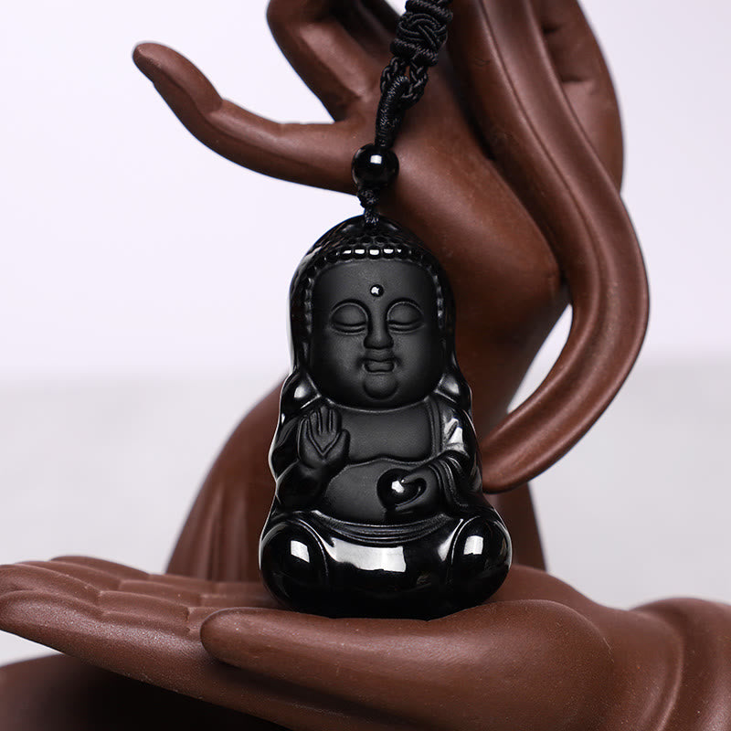Black Obsidian Buddha Necklace - carved black stone pendant displayed on brown ceramic hand prop, 3/4 view, Shielding