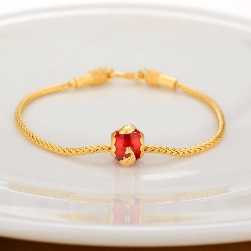 18K Gold Om Mani Padme Hum Koi Fish Bracelet – gold braided chain with translucent red glass bead charm on white ceramic dish, eye-level