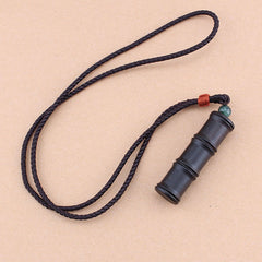 Ebony Wood Bamboo Prayer Box Necklace – Black braided cord necklace with bamboo pendant, red knot and green bead, beige tan background diagonal view