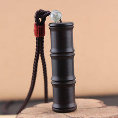 Ebony Wood Bamboo Prayer Box Necklace – Dark bamboo pendant with translucent bead and red cord on natural wood slice base, low three-quarter angle