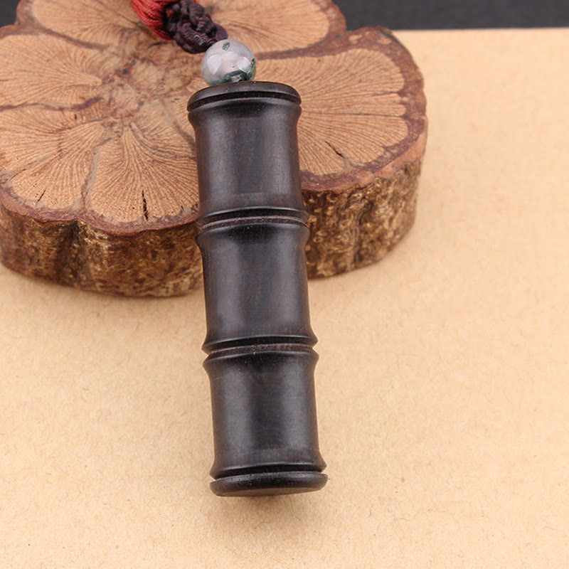 Ebony Wood Bamboo Prayer Box Necklace – Black bamboo-segment pendant with green bead and red accent detail shot, beige surface with wood slice backdrop