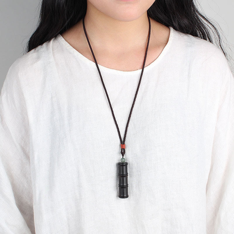 Ebony Wood Bamboo Prayer Box Necklace – Black bamboo pendant with green bead and red cord worn on white shirt at chest level, neutral gray lifestyle