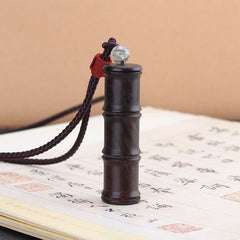 Ebony Wood Bamboo Prayer Box Necklace – Dark bamboo-segment pendant on cord with jade bead and red wrap, Chinese calligraphy book backdrop, low angle