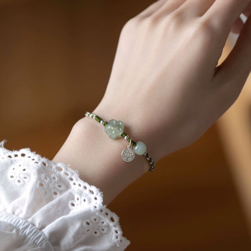 Plum Blossom Jade Flower Braided Bracelet – Jade flower bead with white pearl accents and silver longevity charm on green braided cord worn with white lace sleeve, wood background
