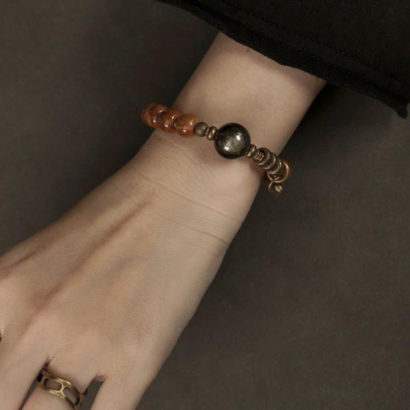 Tiger Eye Obsidian Wealth Bracelet – Product photo on gray surface showing brown beaded bracelet with metal accents