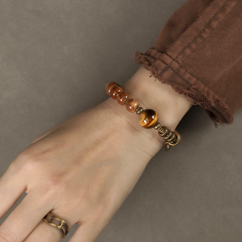 Tiger Eye Obsidian Wealth Bracelet – Wrist close-up with brown beads, tiger's eye focal and matching brass ring, neutral gray background
