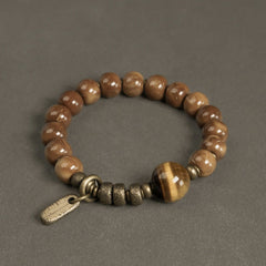 Tiger Eye Obsidian Wealth Bracelet – Polished brown beads with tiger's eye focal stone and brass spacers on gray textured surface