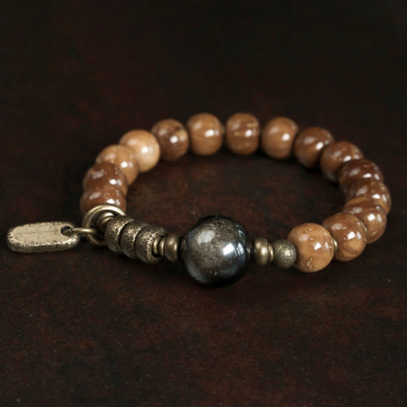 Tiger Eye Obsidian Wealth Bracelet – Tan stone beads with dark metallic gunmetal focal bead on dark brown wood grain surface