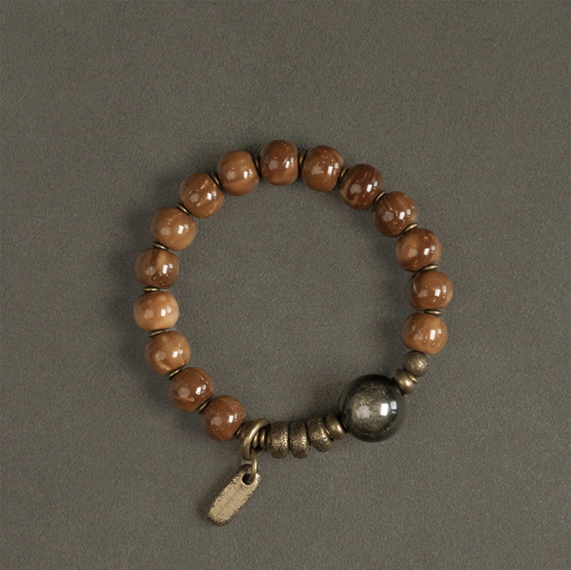 Tiger Eye Obsidian Wealth Bracelet – Amber-brown resin beads with dark metal sphere and brass spacer beads on gray textured surface
