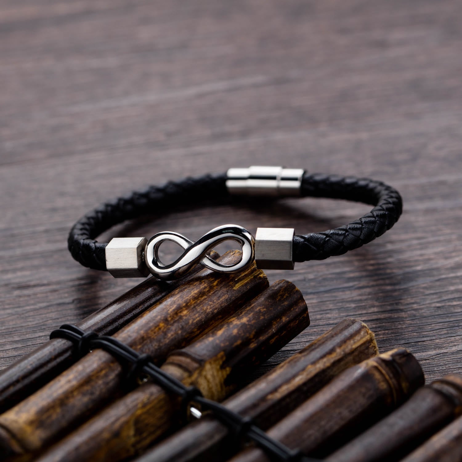 Endless Knot Titanium Steel Leather Bracelet – Silver infinity leather bracelet on weathered bamboo sticks with dark wood grain, rustic styling