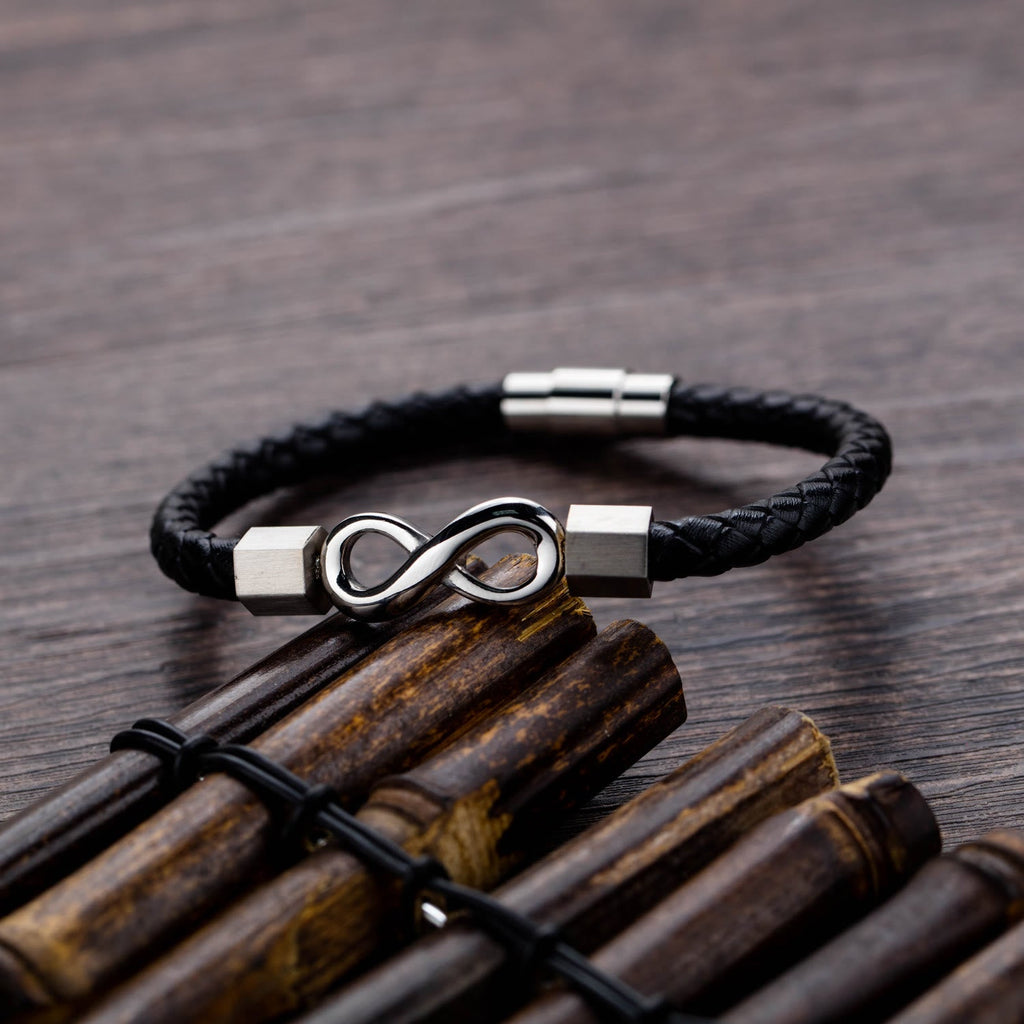 Endless Knot Titanium Steel Leather Bracelet – Silver infinity leather bracelet on weathered bamboo sticks with dark wood grain, rustic styling