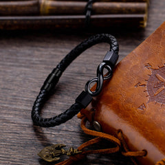 Endless Knot Titanium Steel Leather Bracelet – Black leather with matte infinity clasp on compass-embossed brown leather pouch with dark wood and bamboo backdrop