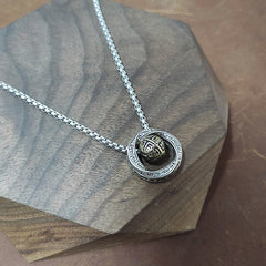 Mobius Copper Wealth Necklace – Silver Mobius pendant with gold sphere resting on dark octagonal wood display, warm brown leather background