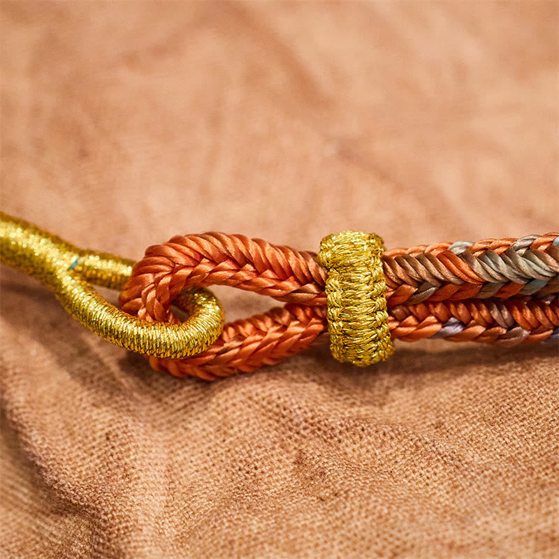 Five-Color Eight Thread Peace Knot Bracelet – Rust-orange multicolored braided cord with metallic gold hook clasp and gold thread wrapping, tan woven fabric macro close-up