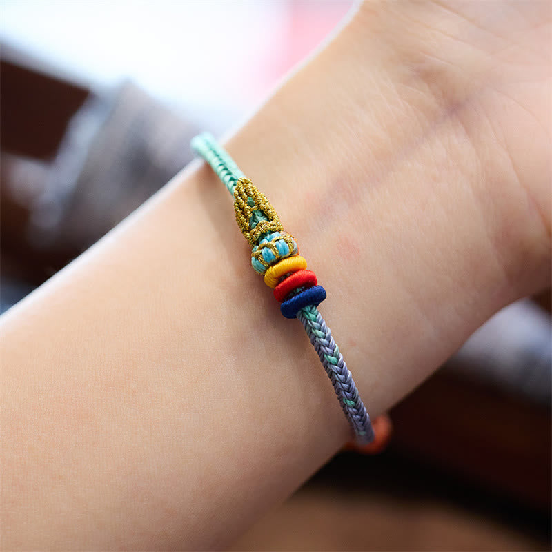 Five-Color Eight Thread Peace Knot Bracelet – Mint green to gray-purple gradient cord with gold knot, turquoise bead and yellow red blue stacked rings worn on wrist