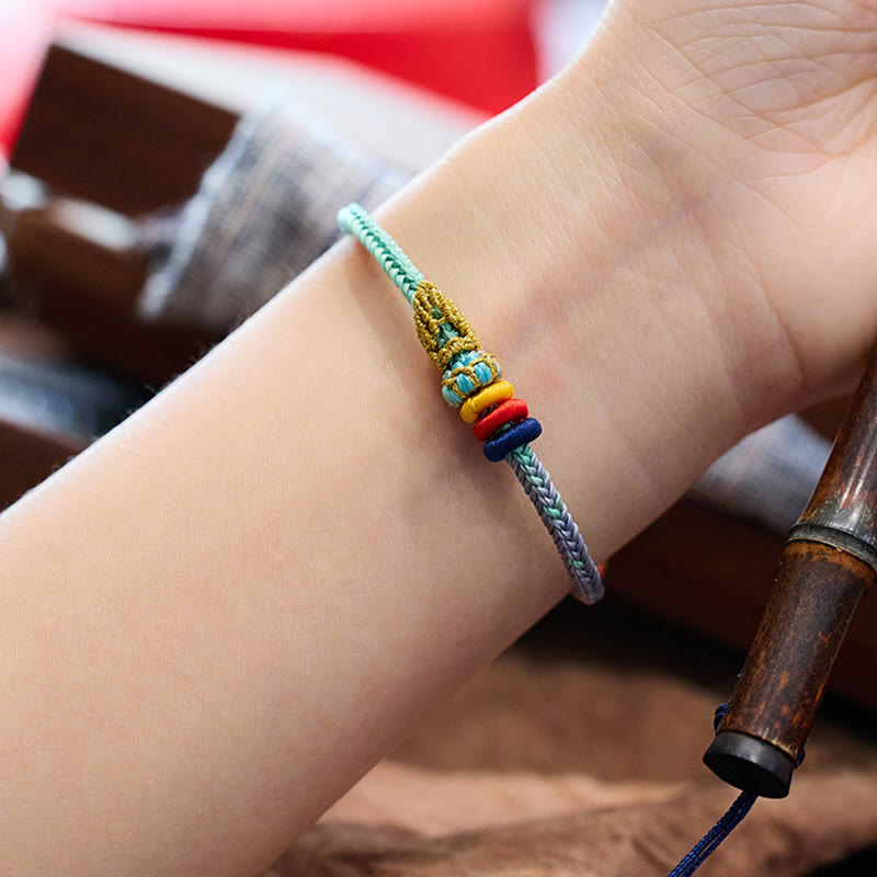 Five-Color Eight Thread Peace Knot Bracelet – Green lavender gradient bracelet with gold-threaded knot and multicolored bead stack worn on wrist, warm wood blur background