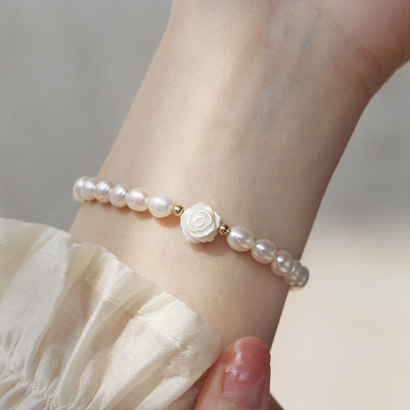 Natural Pearl Sincerity Bracelet – White pearl beads on silver chain with gold leaf charms, pink lavender floral background soft bokeh, elevated side angle