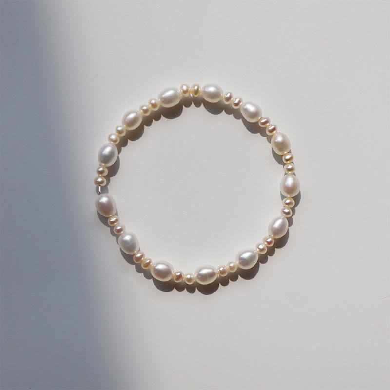 Natural Pearl Sincerity Bracelet – White pearl bead bracelet with gold leaf charms on silver chain, pink rose garden background lifestyle shot, side angle