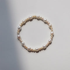 Natural Pearl Sincerity Bracelet – White pearl bead bracelet with gold leaf charms on silver chain, pink rose garden background lifestyle shot, side angle