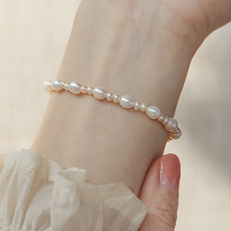 Natural Pearl Sincerity Bracelet – White pearl beads on silver chain bracelet worn on wrist, soft pink floral blurred background, lifestyle side view
