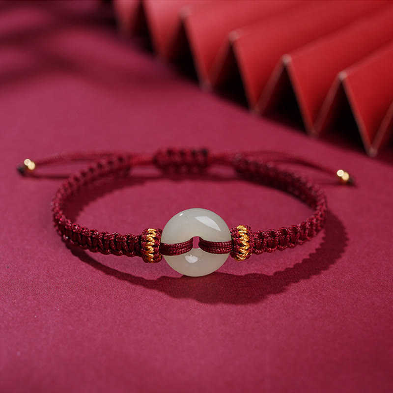 Peace Buckle Jade Abundance Bracelet – Red cord bracelet with jade peace buckle flanked by gold rings and adjustable knot closure, red paper fan backdrop, low angle