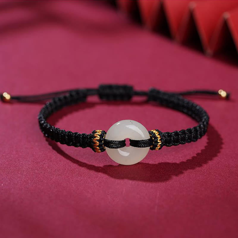 Peace Buckle Jade Abundance Bracelet – Black braided cord with translucent white jade peace buckle and gold-tipped ends, deep magenta fabric with fan elements, front angle