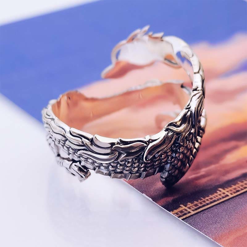 Vintage Dragon Pattern Silver Ring – Silver dragon ring with feathered wing segments and ornate head, peachy orange and blue dual-tone printed background, low angle