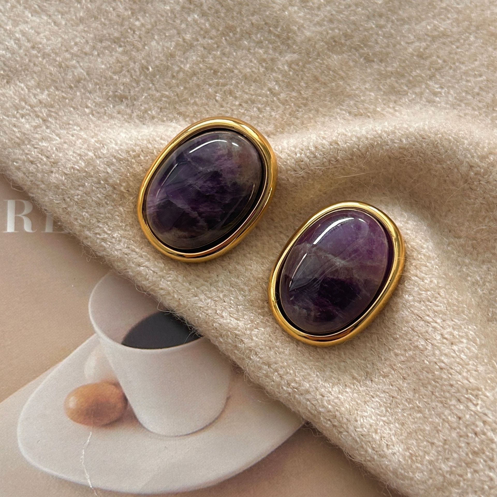 Amethyst Stud Earrings – oval purple amethyst cabochons in gold bezel setting on cream knit sweater with magazine props, crystal earrings
