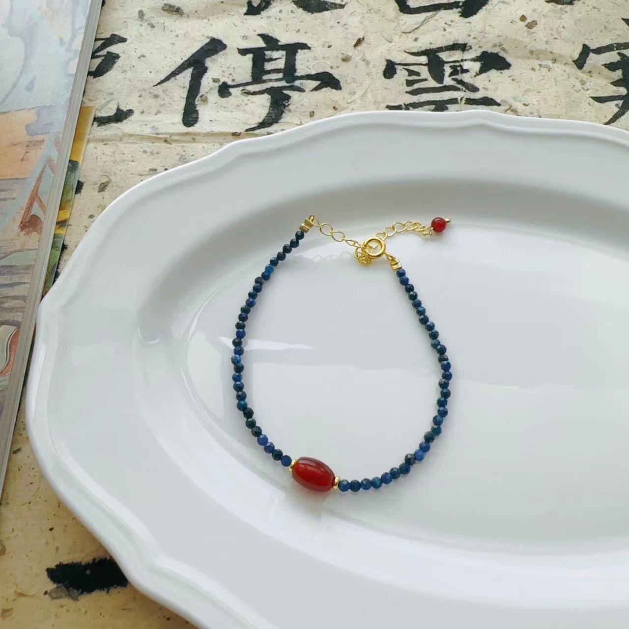 Lapis Lazuli Agate Bracelet – delicate blue lapis chain with single red agate barrel bead and gold lobster clasp on white plate