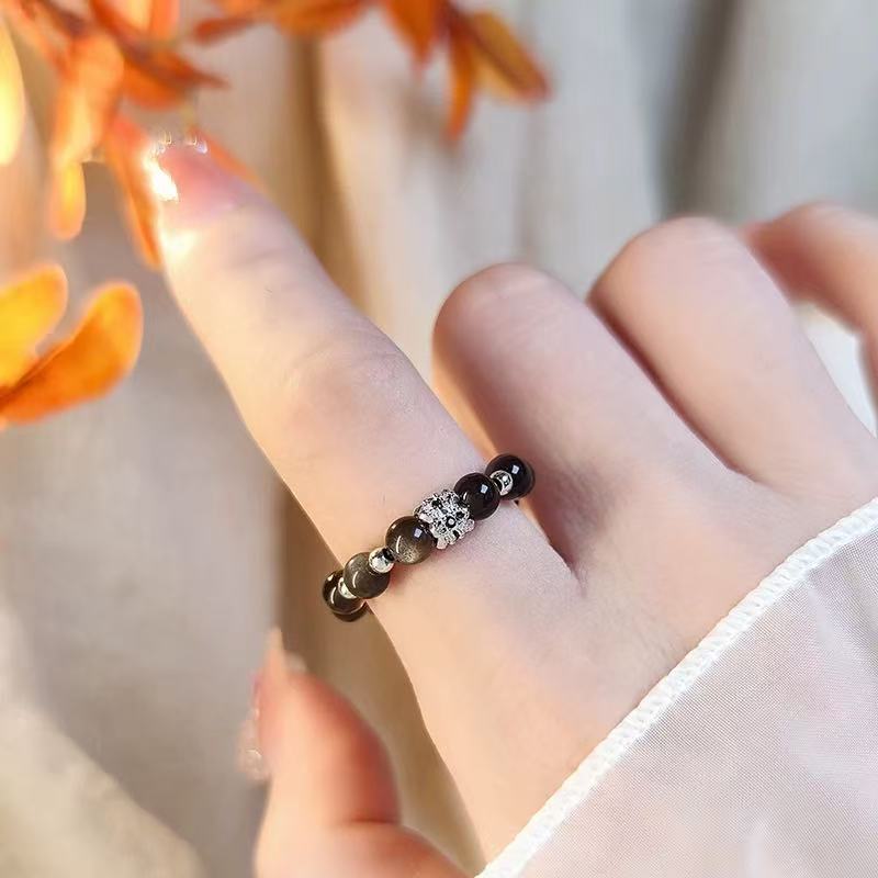 Obsidian Crown Ring – Black obsidian bead ring with silver cz crown charm worn on finger, autumn leaf background