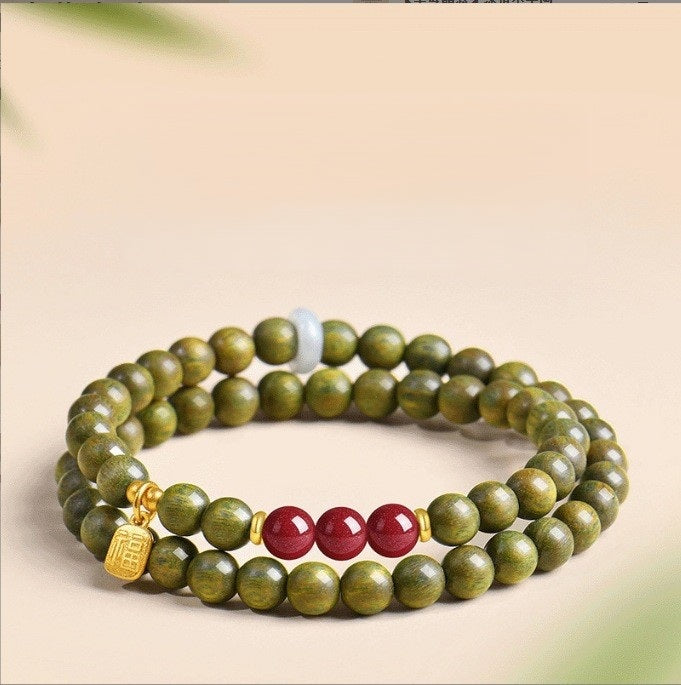 Green Sandalwood Bracelet – Double wrap with dark red beads and gold fortune charm on beige, wood