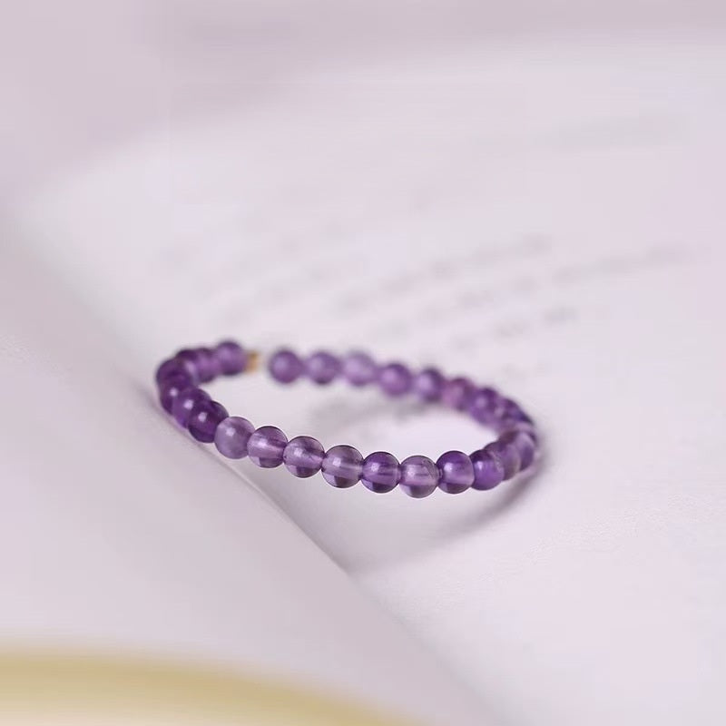 Amethyst Ring – Purple amethyst bead ring resting on open book pages, calming crystal jewelry