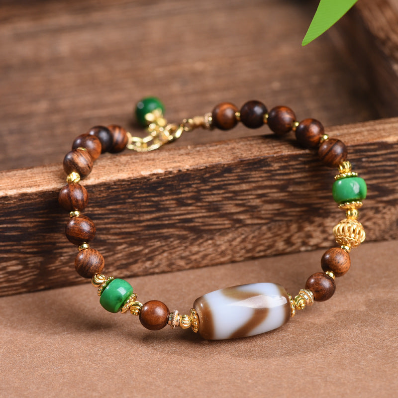 Dzi Rosewood Bracelet – Rosewood beads with Tibetan dzi centerpiece on wooden plank, green accent stones