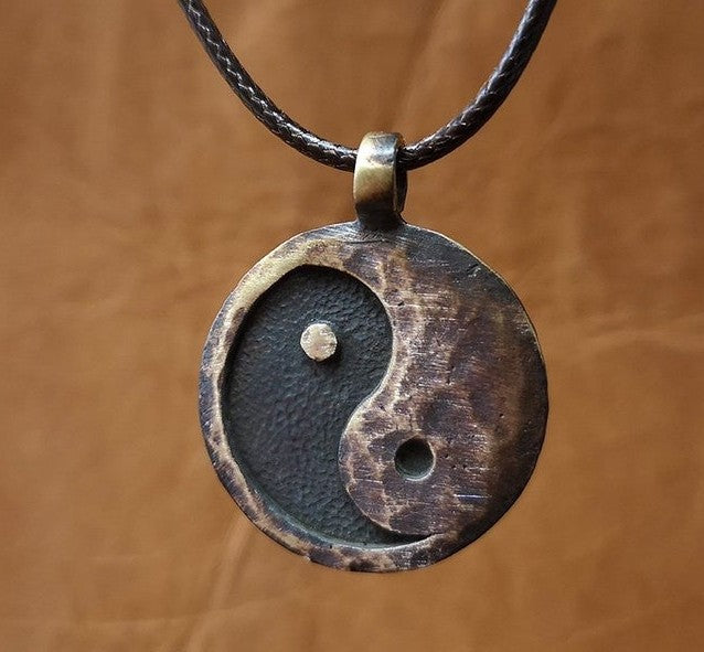 Yin Yang Pendant – antique bronze circular pendant on black braided cord, warm brown leather background