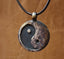 Yin Yang Pendant – antique bronze circular pendant on black braided cord, warm brown leather background