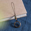 Sandalwood Phone Grip – Single green sandalwood ring lanyard with orange accent bead on book and blue cloth, wooden phone strap