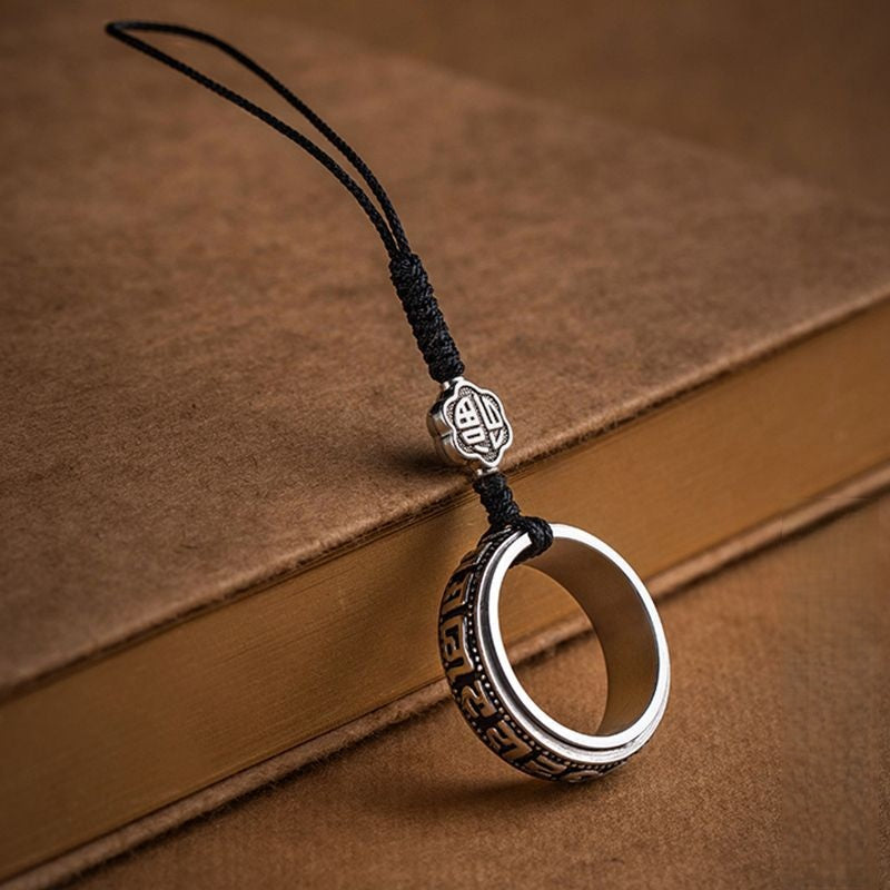 Mantra Phone Ring – silver spinning ring with black cord on vintage brown book, engraved symbols