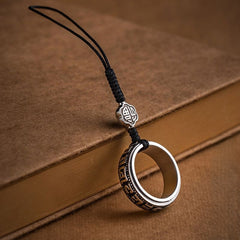 Mantra Phone Ring – silver spinning ring with black cord on vintage brown book, engraved symbols
