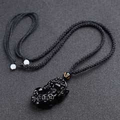 Obsidian Pixiu Necklace – Black braided cord with carved obsidian pixiu, white bead adjusters on gray, feng shui